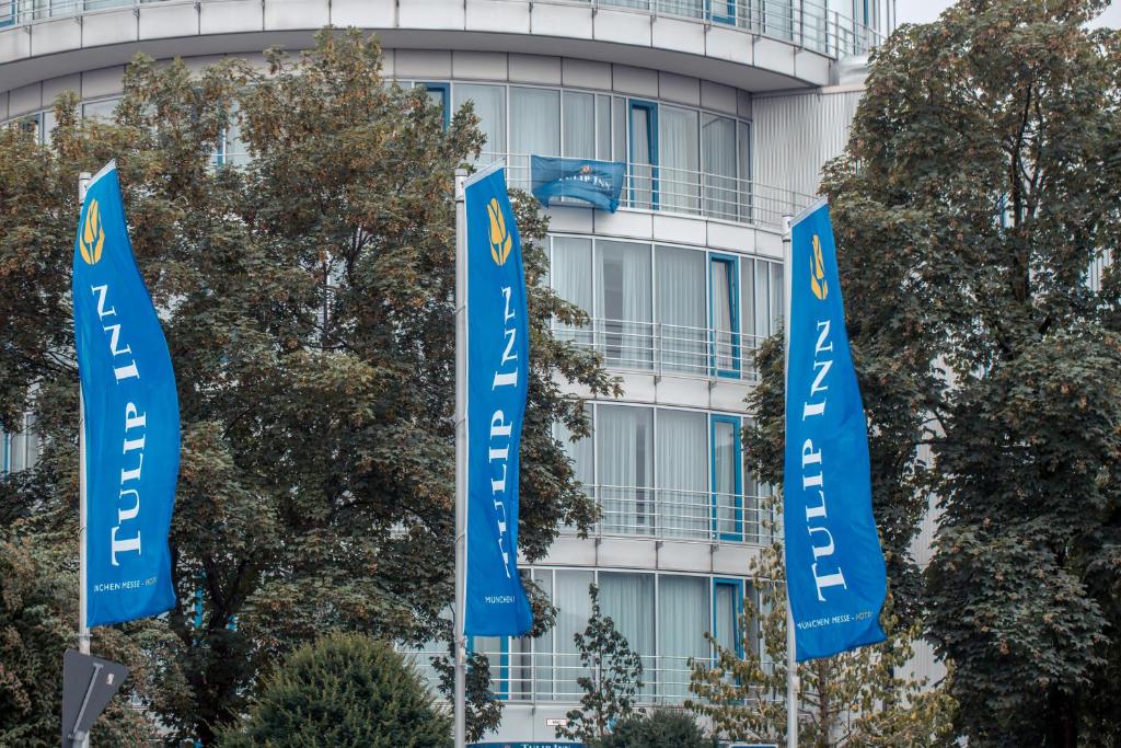 drei blaue Flaggen vor einem Gebäude in der Unterkunft Tulip Inn München Messe in München