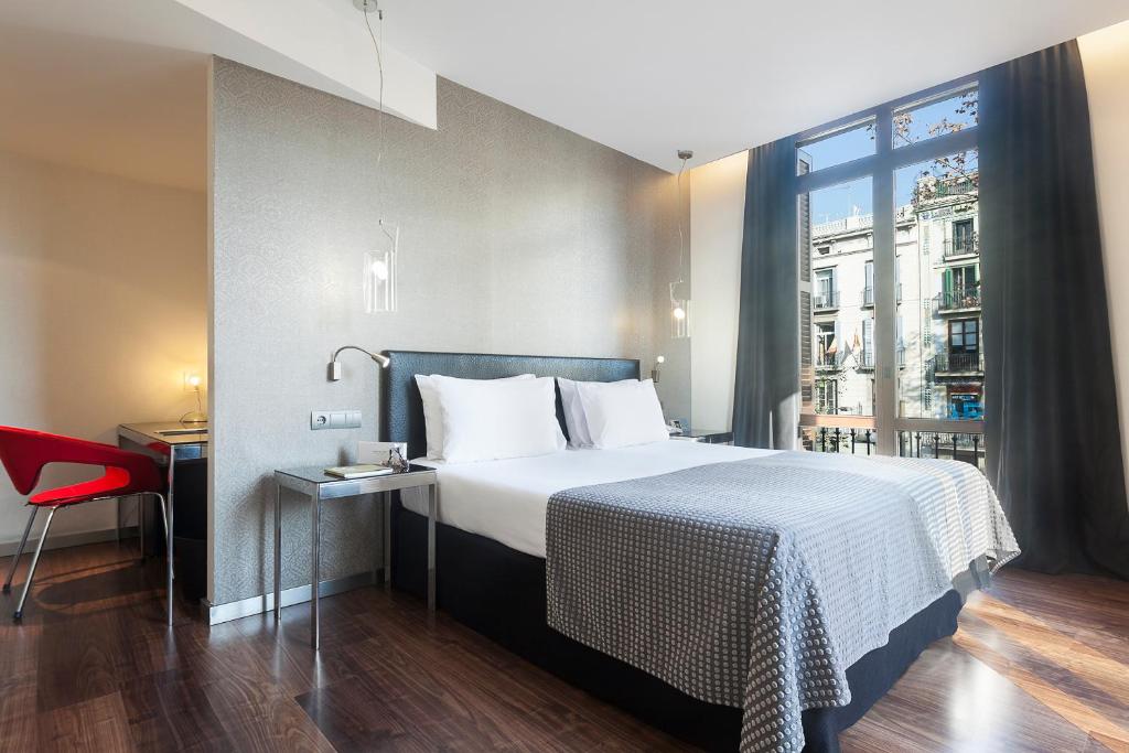 a hotel room with a bed and a desk and a window at Exe Ramblas Boquería in Barcelona