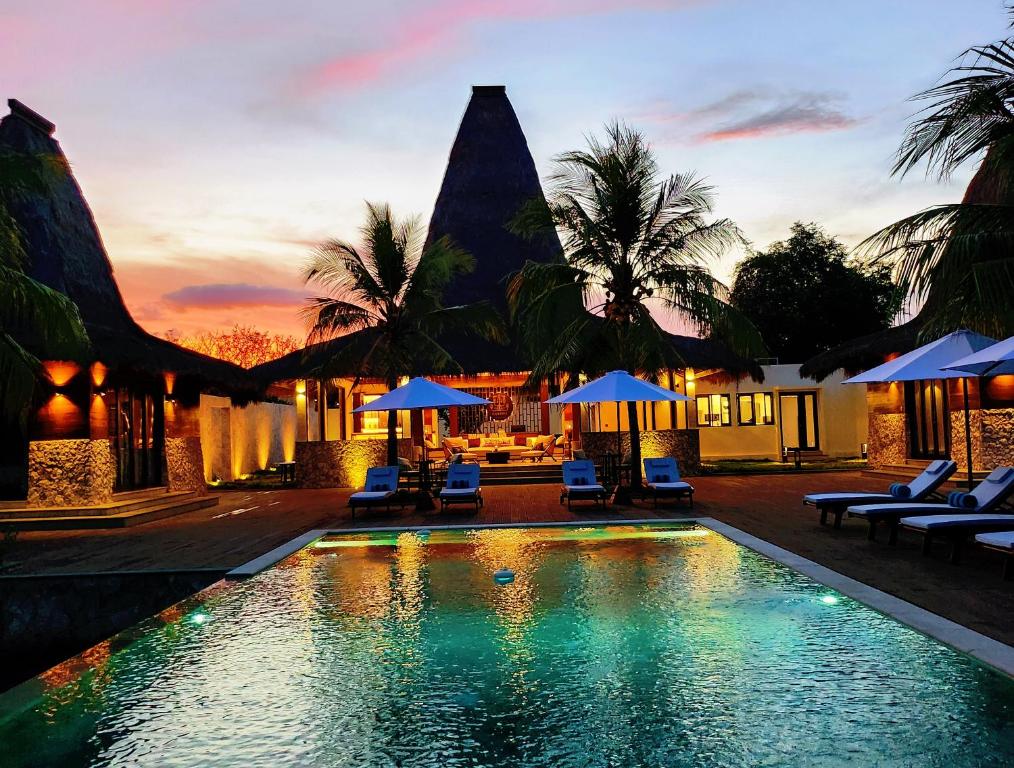 a resort pool with chairs and umbrellas at sunset at KANDORA Luxury villas in Maujawa