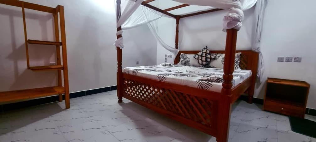 een slaapkamer met een houten bed met een hemelbed bij Malkia Apartment in Kibigija