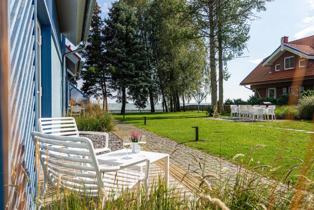 a patio with white chairs and a table on the side of a house at Saulės apartamentai su vaizdu į Kušių marias in Neringa
