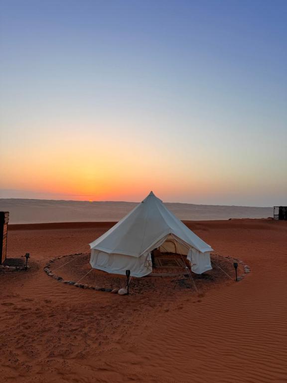 une tente sur la plage avec le coucher de soleil en arrière-plan dans l'établissement Bedouin Stars, à Ḩawīyah