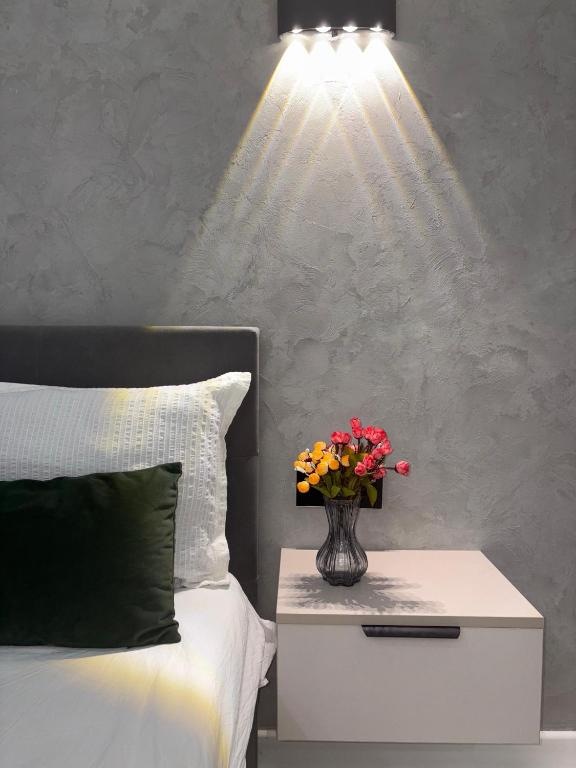 eine Vase mit Blumen auf einem Nachttisch neben einem Bett in der Unterkunft Comfort Studio Apartment in Almaty