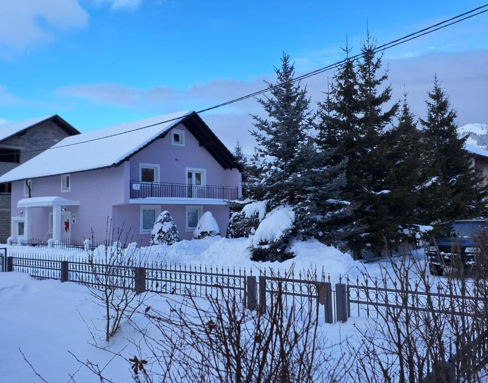 a white house with a fence in the snow at Apartmani Biser Kupresa 2 in Kupres