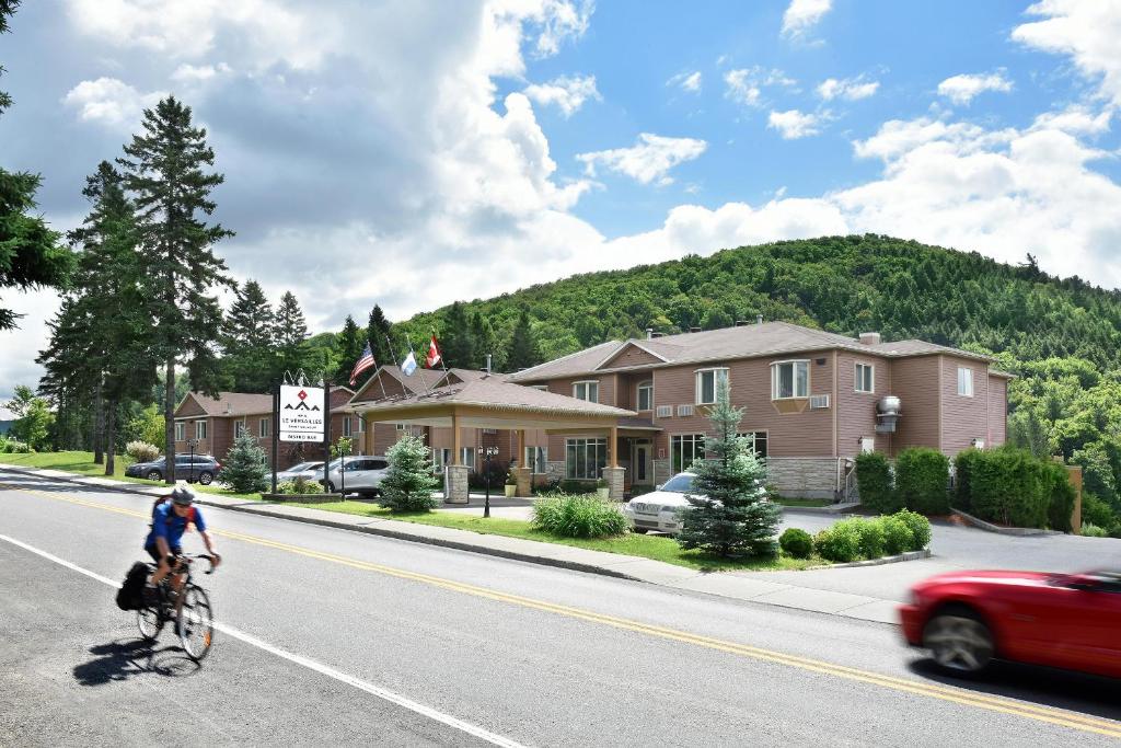 a person riding a bike down a street with a red car at Hotel Le Versailles in Saint-Sauveur-des-Monts