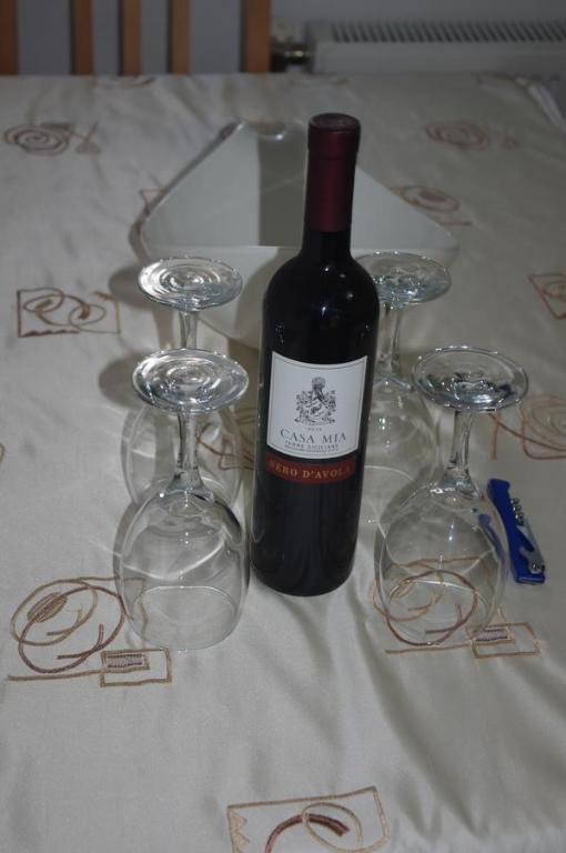 a bottle of wine and four wine glasses on a table at Apartment Emma in Sarajevo