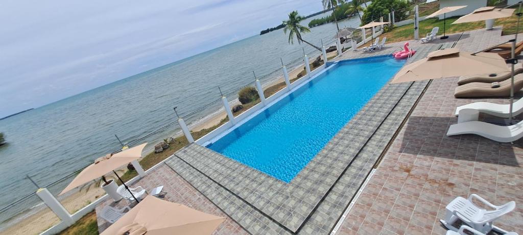a swimming pool next to the ocean with umbrellas at Chilly Beach Resort Palawan in Aborlan