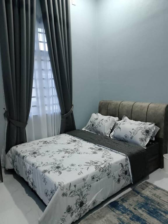 a bed with a black and white comforter and a window at HomeStay Rafiza in Jertih