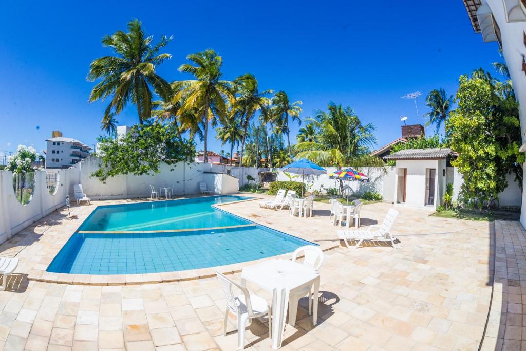 a pool with tables and chairs and palm trees at Vila do Galo in Porto De Galinhas