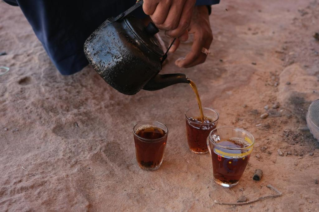 a person pouring a drink into two glasses at Sunrise Magic Camp in Wadi Rum