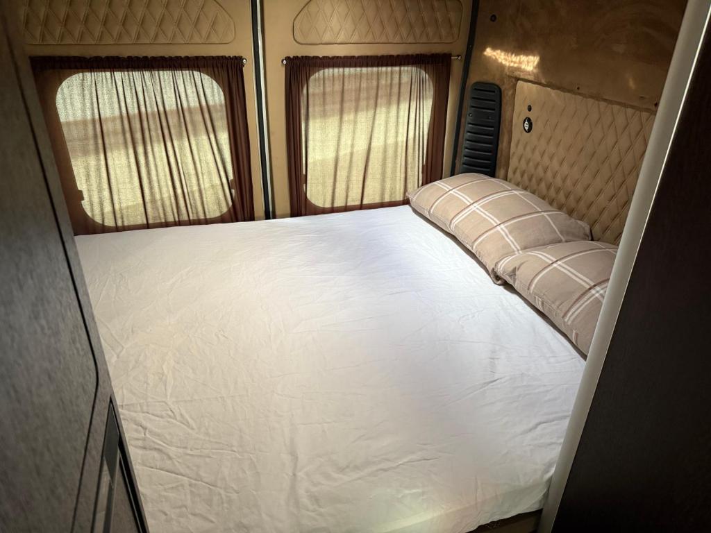 a large white bed in an rv with two windows at Hotel auf Räder in Wangen im Allgäu