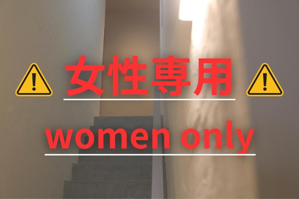 un panneau indiquant « Femmes seulement » avec des panneaux de danger et des escaliers dans l'établissement 2times Dormitory Hotel, à Itoshima
