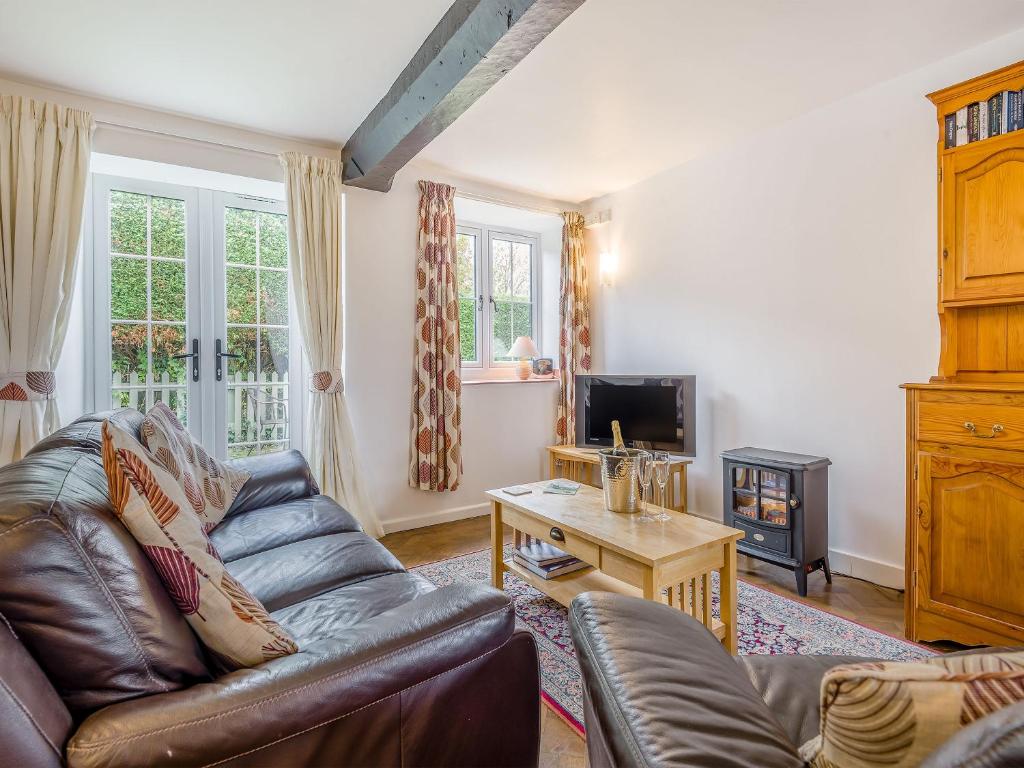 a living room with a leather couch and a tv at Horseshoe Cottage-Uk37360 in Lympsham