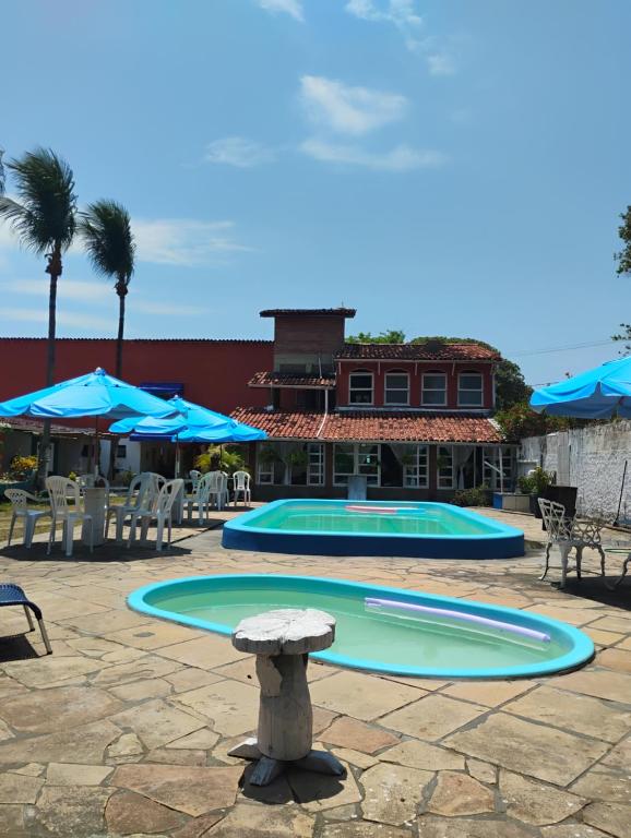 a swimming pool with blue umbrellas and a table at POUSADA VILA DE ATALAIA OFlCIAL in Canavieiras