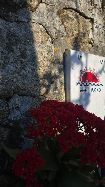 a sign on a stone wall next to red flowers at Mirada Do Roxo in Oia