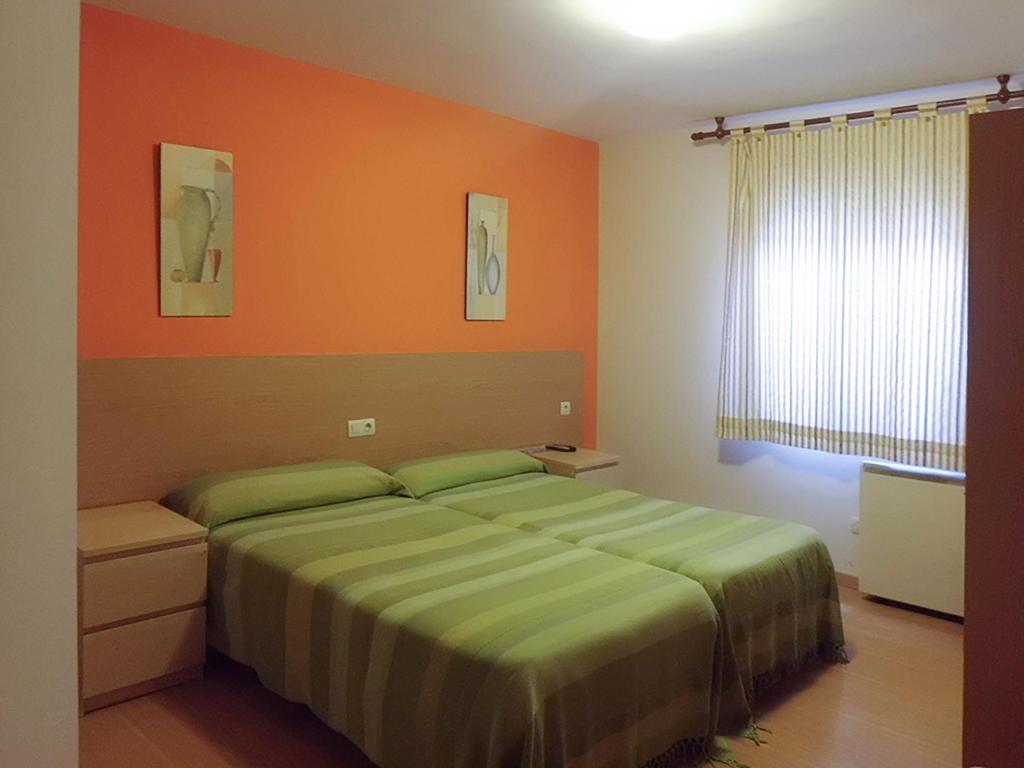 a bedroom with a bed with an orange wall at Hostal Caracas in Lalín