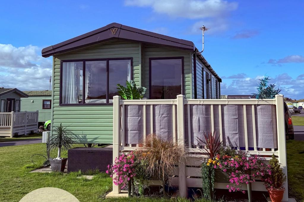 a green tiny house with a white fence at Dune View Caravan in Ynys-lâs Station