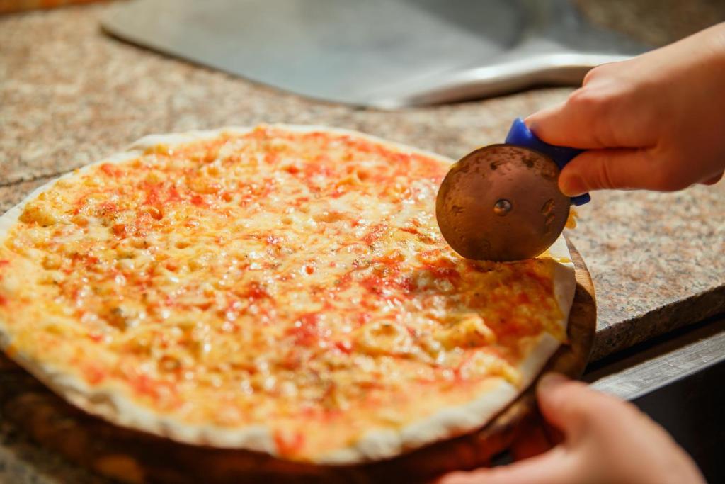 uma pessoa a cortar uma pizza com um cortador de pizza em Mini Hotel Venezia em Atyraū