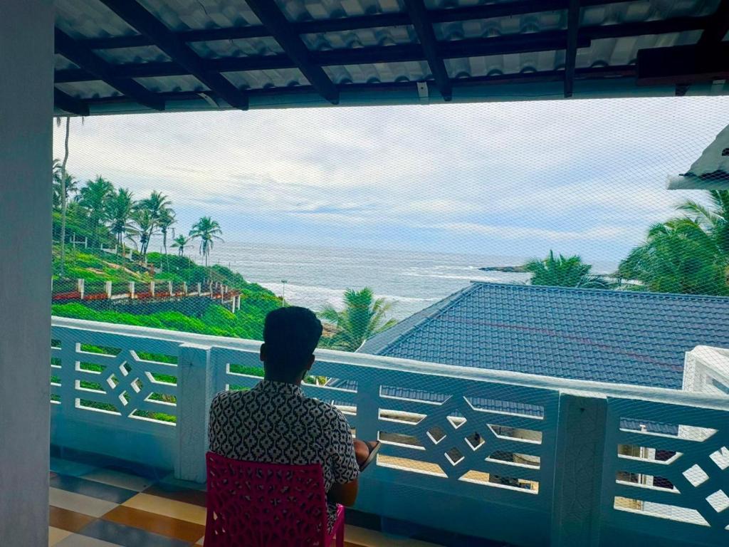 a woman sitting on a balcony looking out at the ocean at Hotel Paradise Kovalam in Trivandrum