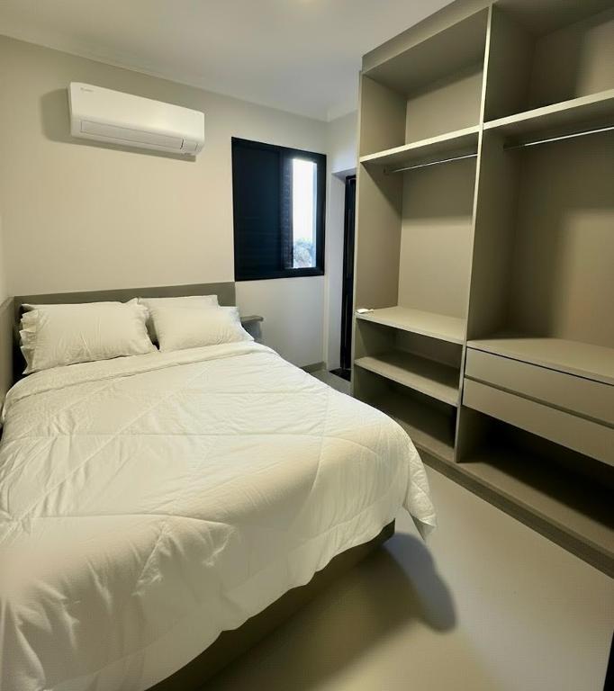a bedroom with a large white bed and shelves at Studio Maia Aconchego e praticidade 190m da UFU in Uberlândia