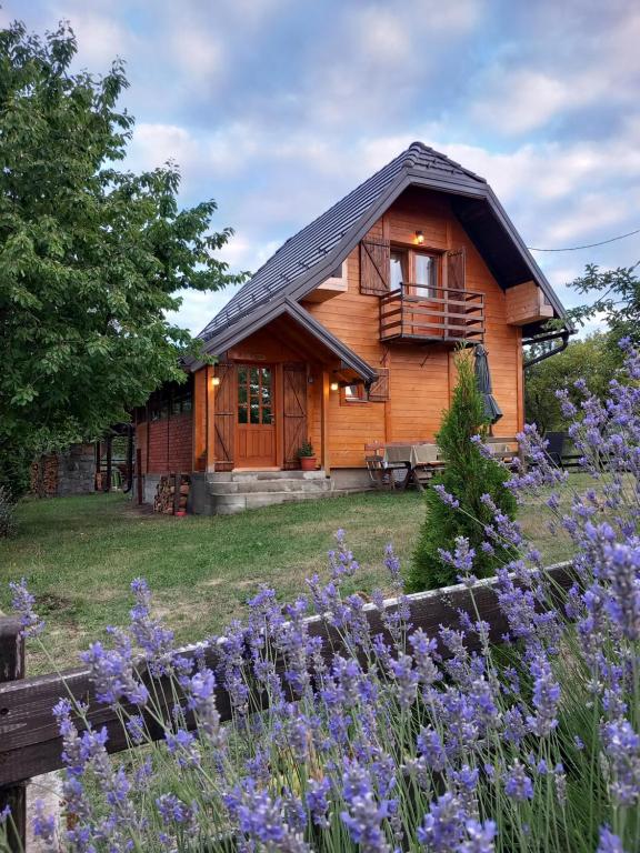 a wooden cabin with purple flowers in front of it at Brvnare Na Brdu in Šljivovica