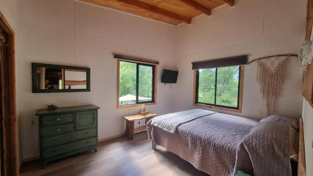 ein Schlafzimmer mit einem Bett, einer Kommode und zwei Fenstern in der Unterkunft Cabaña y hostal antupiren 