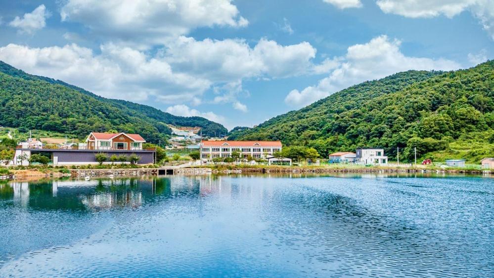 a village on a lake with mountains in the background at Glamdog Dog Pension Tongyeong Branch in Wŏnmul-li
