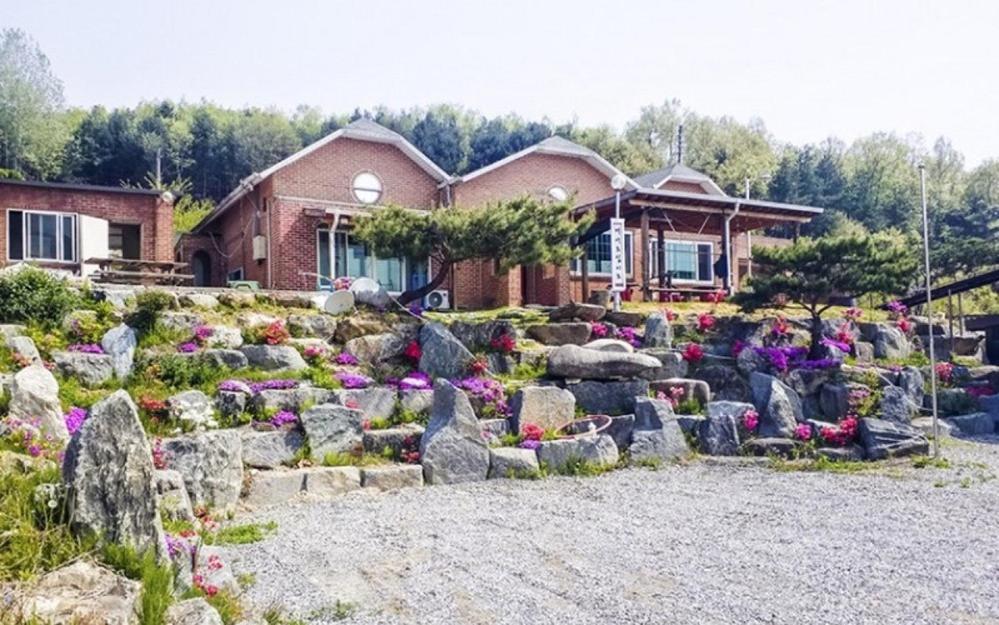 a house with a garden of flowers and rocks at Choongju Garden Arirang Pension in Chungju