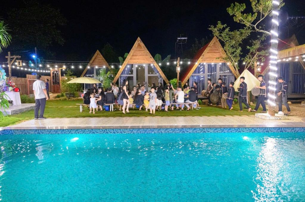 Hồ Bình Yên Homestay&Coffee-BBQ في Plei Kơtêng: مجموعة من الناس يجلسون حول حمام السباحة في الليل