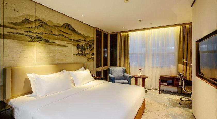 Una habitación de hotel con una cama grande y una silla. en Dahe Jinjiang Hotel, en Zhengzhou