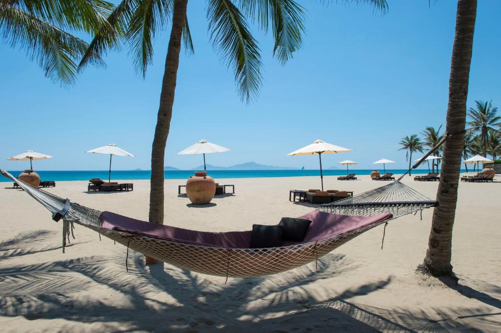 a hammock on a beach with palm trees at Four Seasons The Nam Hai, Hoi An, Vietnam in Hoi An
