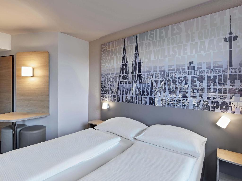 a white bed in a room with a picture on the wall at B&B Hotel Köln-West in Cologne