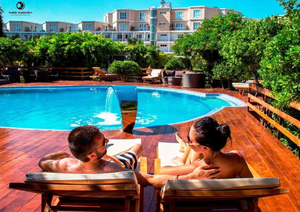 un homme et une femme assis à côté d'une piscine dans l'établissement AF HOTEL AQUAPARK, à Novxanı
