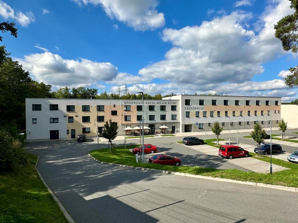 Un gran edificio blanco con coches aparcados en un estacionamiento. en Hotel Prokopávka, en Plzeň