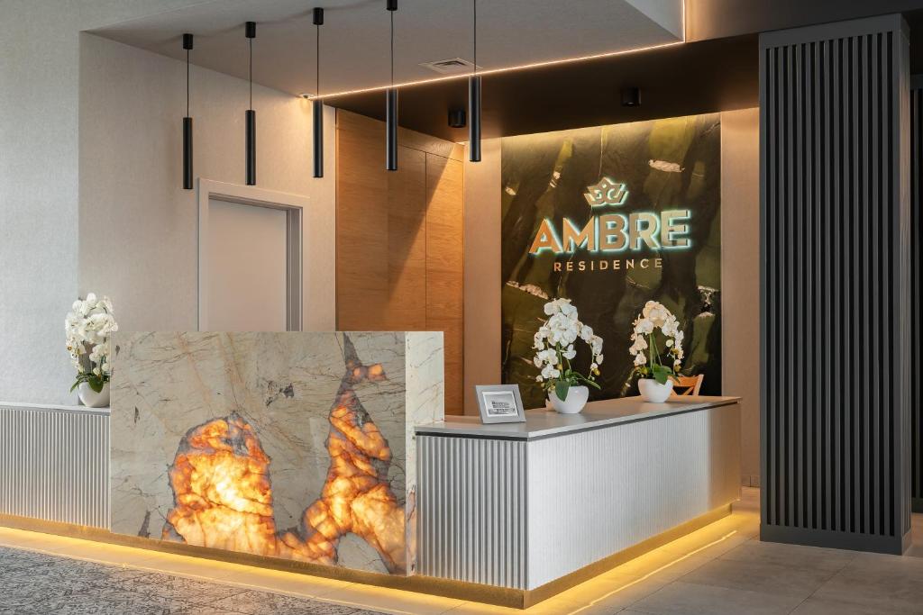 Reception desk with illuminated stone front, AMBRE Residence sign backlit, orchids on the counter.