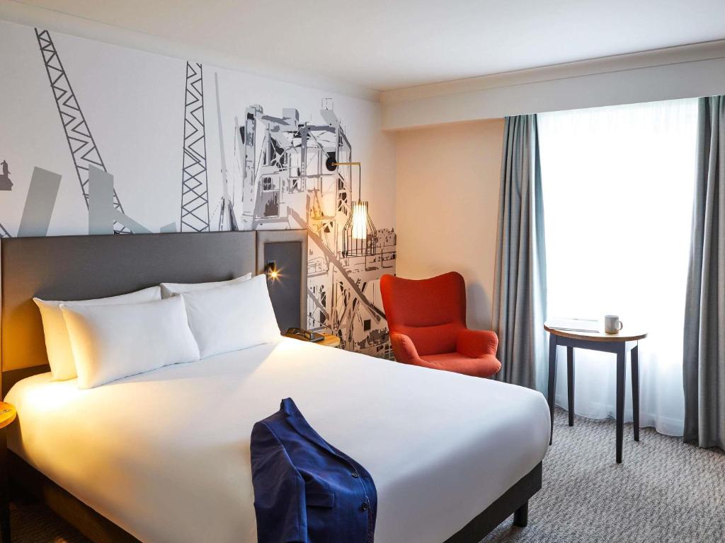a hotel room with a bed and a red chair at Mercure Cardiff in Cardiff