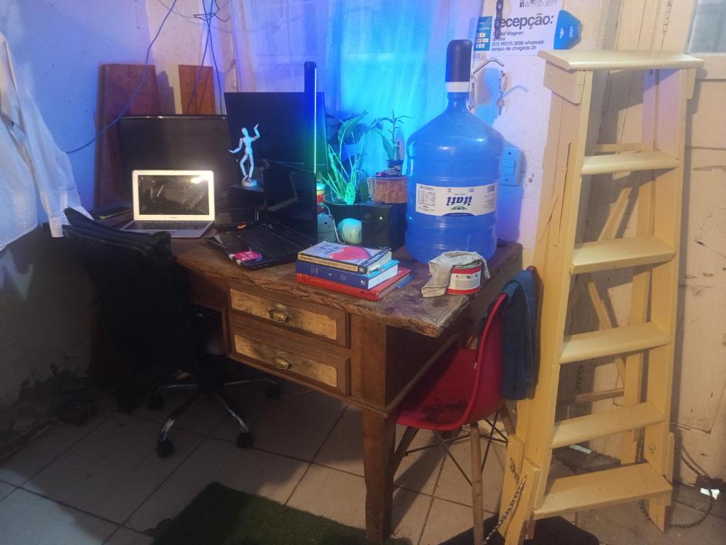 a wooden desk with a bottle of water and a laptop at Cytau Office Wi-fi 3 Estações Trabalho 1 Dormitório Cozinha Sofá in Porto Alegre