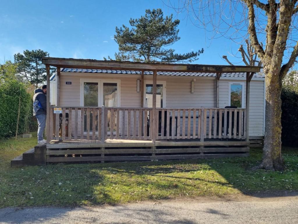 Una pequeña casa con un porche y un hombre parado en el porche. en MH300 le clarys camping 5 étoiles, en Saint-Jean-de-Monts