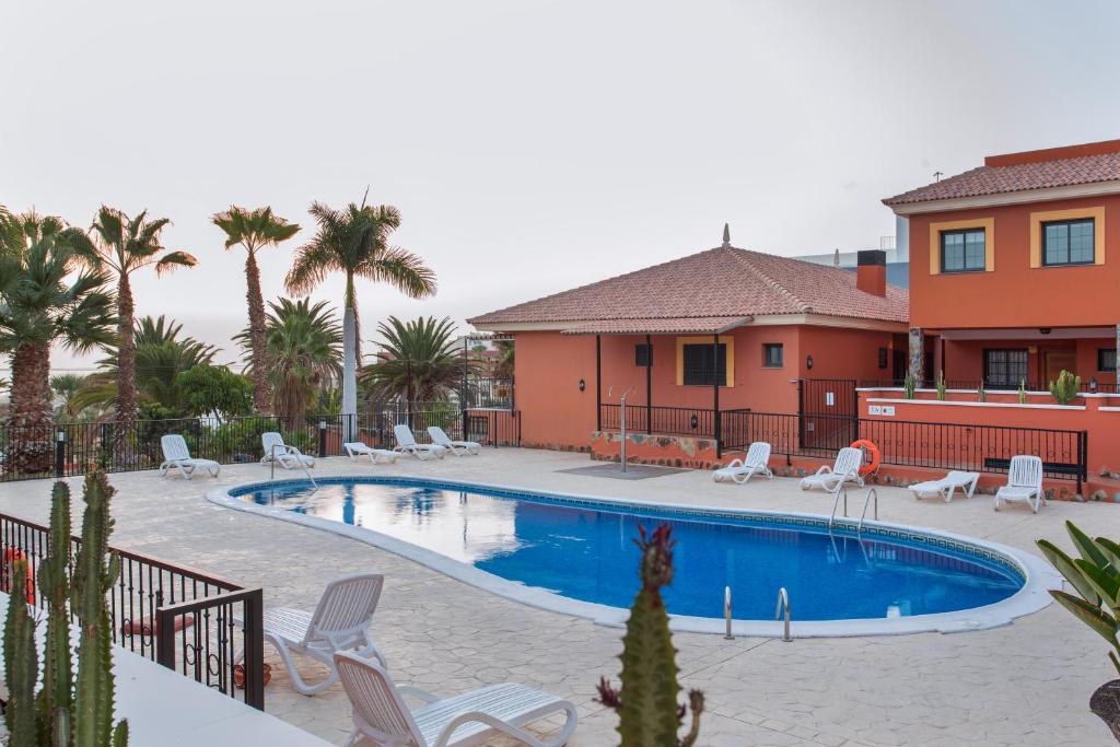 una piscina con sillas y palmeras frente a una casa en Obsidian Aquarela Costa Adeje, en Adeje