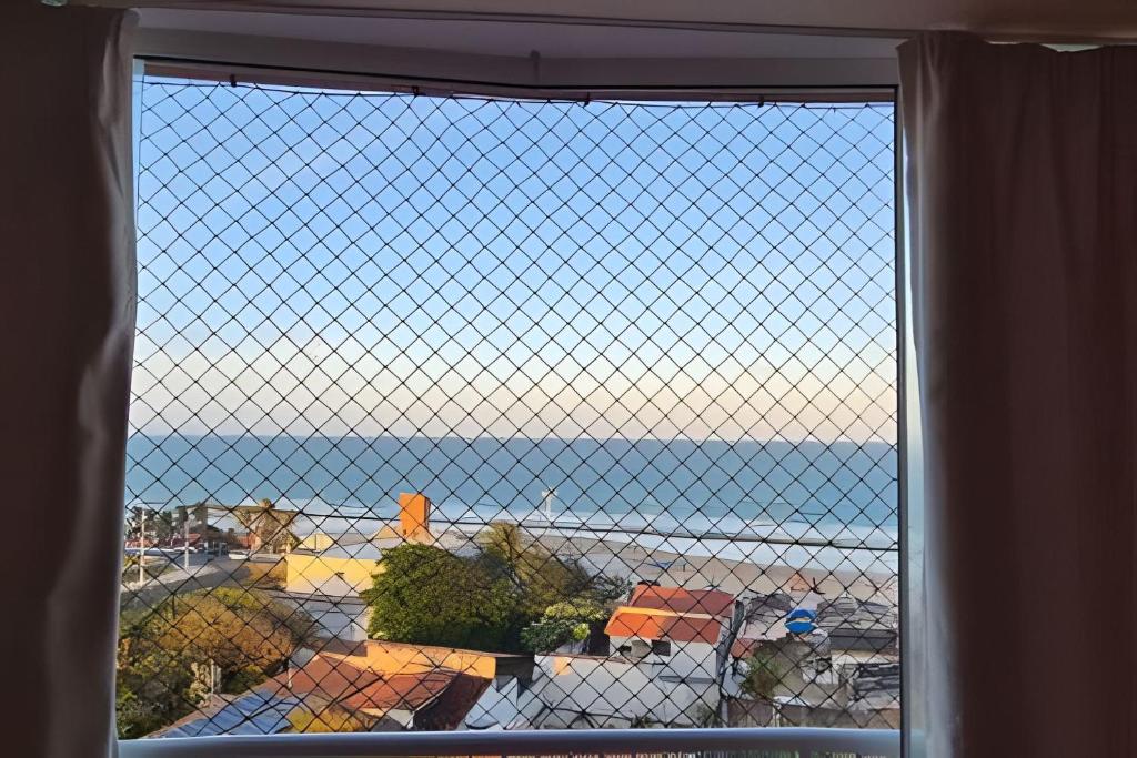 a view of the ocean from a window with a fence at Apartamento brisa do oceano in Natal