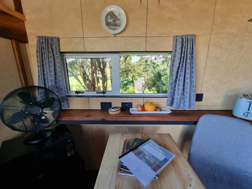 a table with a fan and a window in a caravan at Swiss-Kiwi Cottage and Retreat, B&B in Tauranga