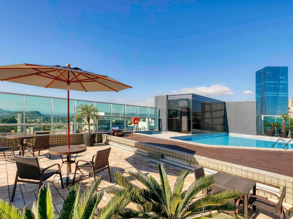 ベロオリゾンテにあるMercure Belo Horizonte Vila da Serraのテーブルとパラソルとプールのあるパティオ