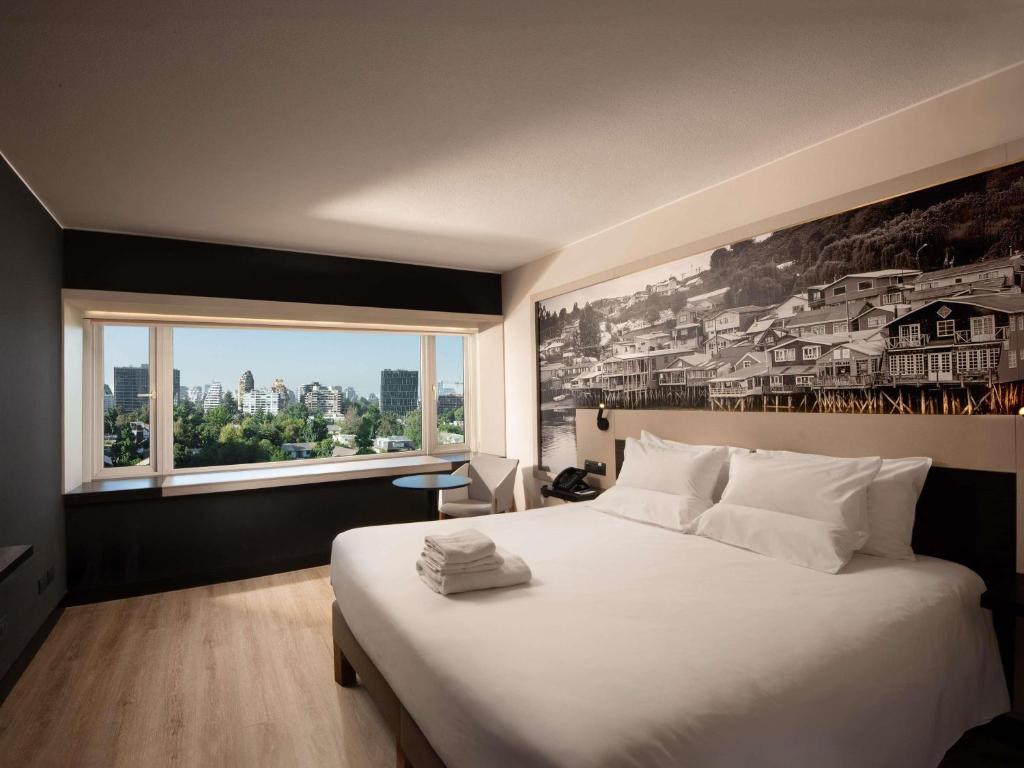 a bedroom with a large white bed with a large window at Novotel Santiago Vitacura in Santiago