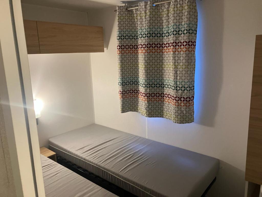 Habitación pequeña con cama y cortina en Mobil home 6 personne, en La Tranche-sur-Mer