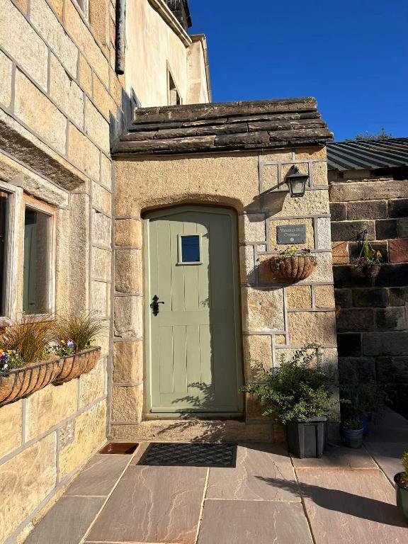 a stone building with a green door on it at Weather Hill Cottage, Hebden Bridge in Hebden Bridge