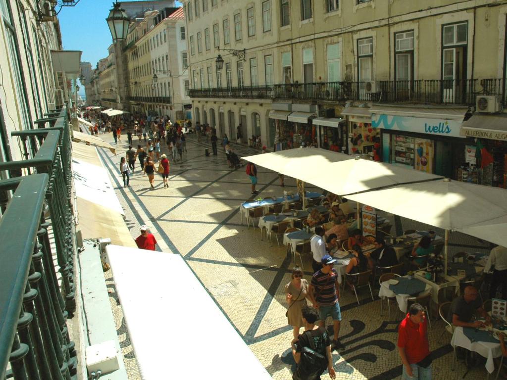 um grupo de pessoas andando em torno de uma rua com mesas e guarda-chuvas em City Center Guest House em Lisboa