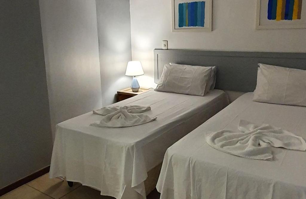 Dos camas en una habitación con sábanas y toallas blancas. en Flat a 450 metros do centro - Praia da Pipa, en Pipa