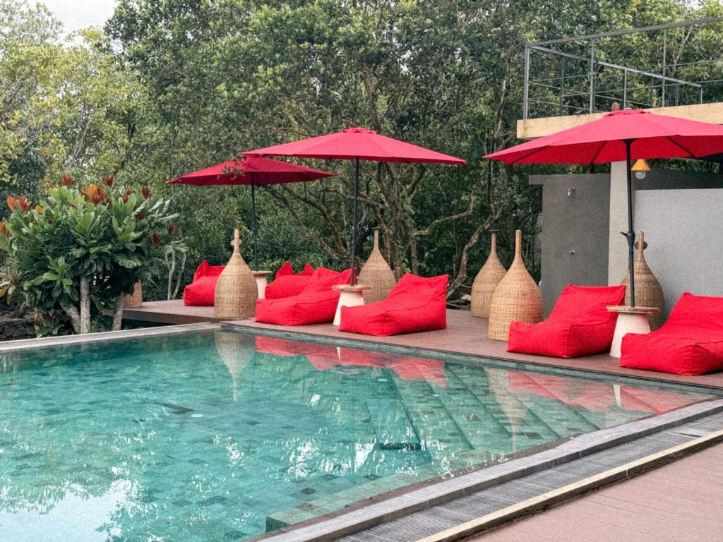 a swimming pool with red pillows and umbrellas next to a swimming pool at Zen Koggala by Sugar Coliving in Habaraduwa