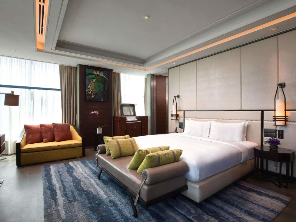A spacious bedroom with a sofa, bench seat, and layered lighting.