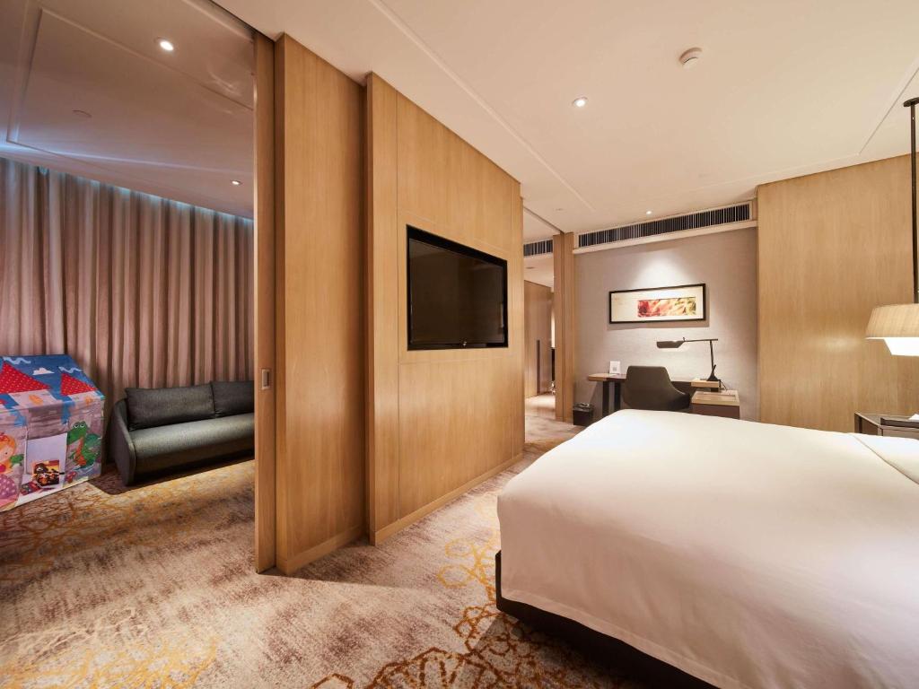 A bedroom with a wall-mounted television, divided sleeping area, and sofa nook.